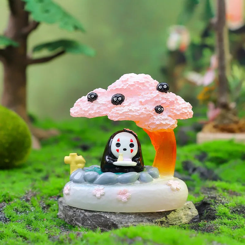 A pink fluffy cloud shaped ornament with black eyes sits on a mossy rock in a natural setting.