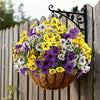 A bouquet of artificial pansy flowers in yellow, purple, and white are displayed in a woven basket hanging on a wooden fence.