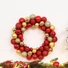 A wreath made of shiny red and gold Christmas ball ornaments on a green pine branch.