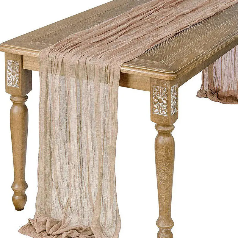 A semi-sheer gauze table runner in sage green draped over a wooden table.