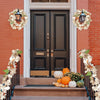 A black front door surrounded by white trim and decorated with artificial maple leaf garlands and pumpkins.