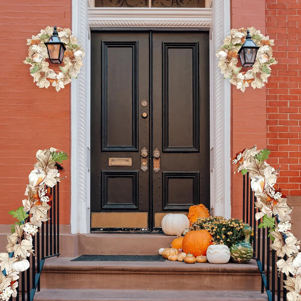 A black front door surrounded by white trim and decorated with artificial maple leaf garlands and pumpkins.