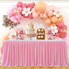 A pink pleated polyester table skirt decorated with balloons and flowers for a party setting.