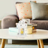 A white vintage hanging metal lantern with a yellow candle sits on a light wood table.