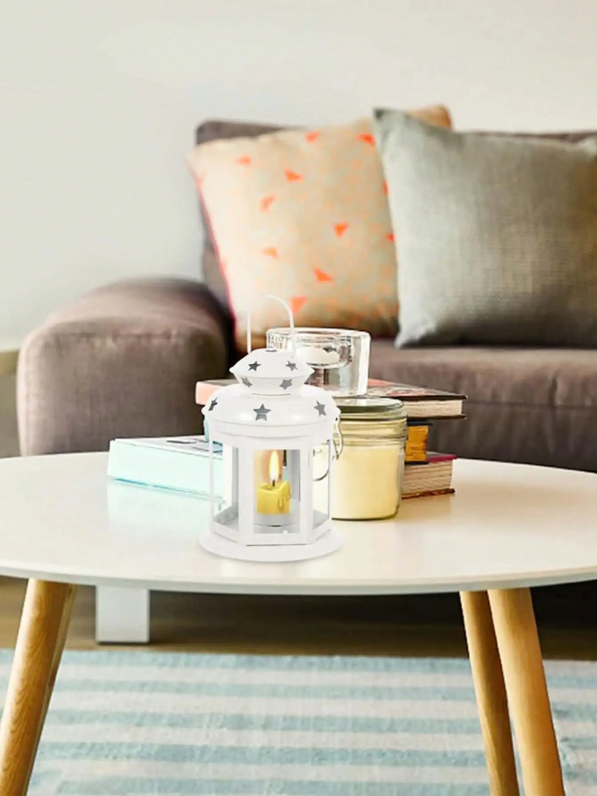 A white vintage hanging metal lantern with a yellow candle sits on a light wood table.