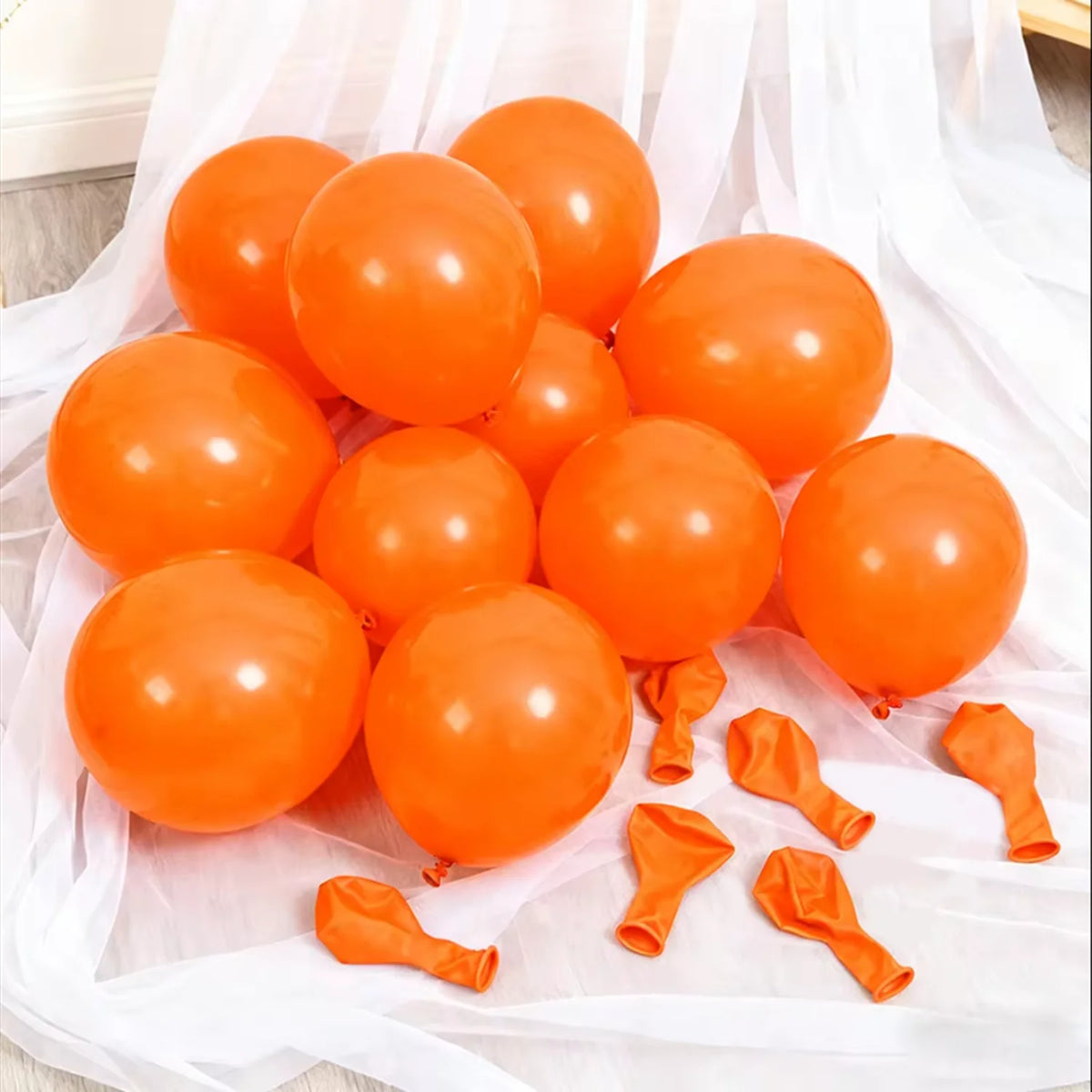 A cluster of bright orange latex balloons scattered on white sheer fabric.