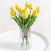 A bouquet of yellow artificial tulip flowers in a clear glass vase on a white surface.