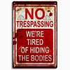 A vintage-style metal sign with red and white lettering that reads NO TRESPASSING WE ARE TIRED OF HIDING THE BODIES