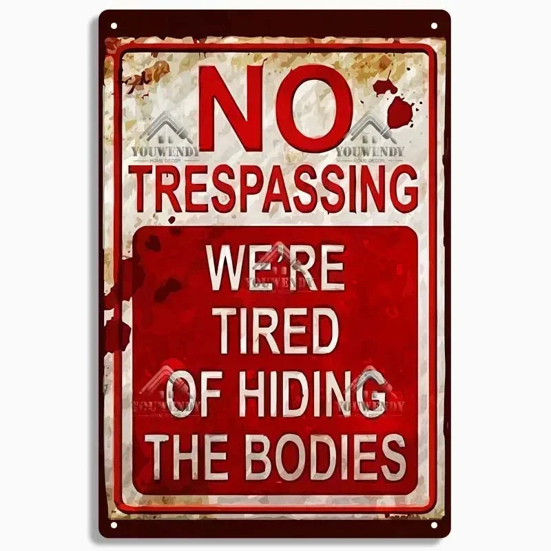 A vintage-style metal sign with red and white lettering that reads NO TRESPASSING WE ARE TIRED OF HIDING THE BODIES