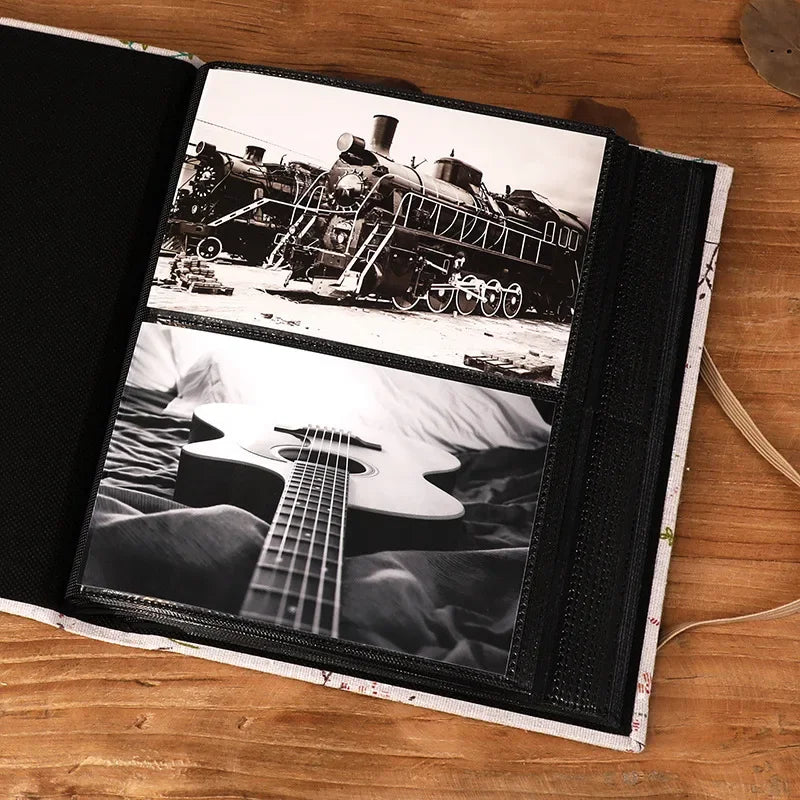 A black linen photo album open to display two black and white photographs: a steam train and an acoustic guitar.