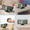 A black LED digital projection alarm clock is shown in various settings, including on a table and near a bed.