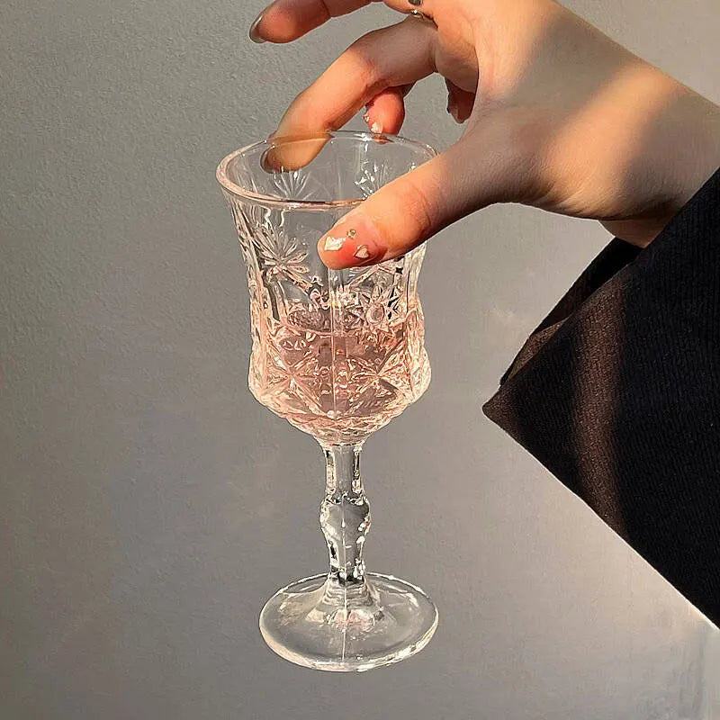 A hand is holding a vintage French-style high-footed wine glass, showcasing its intricate cut glass design.