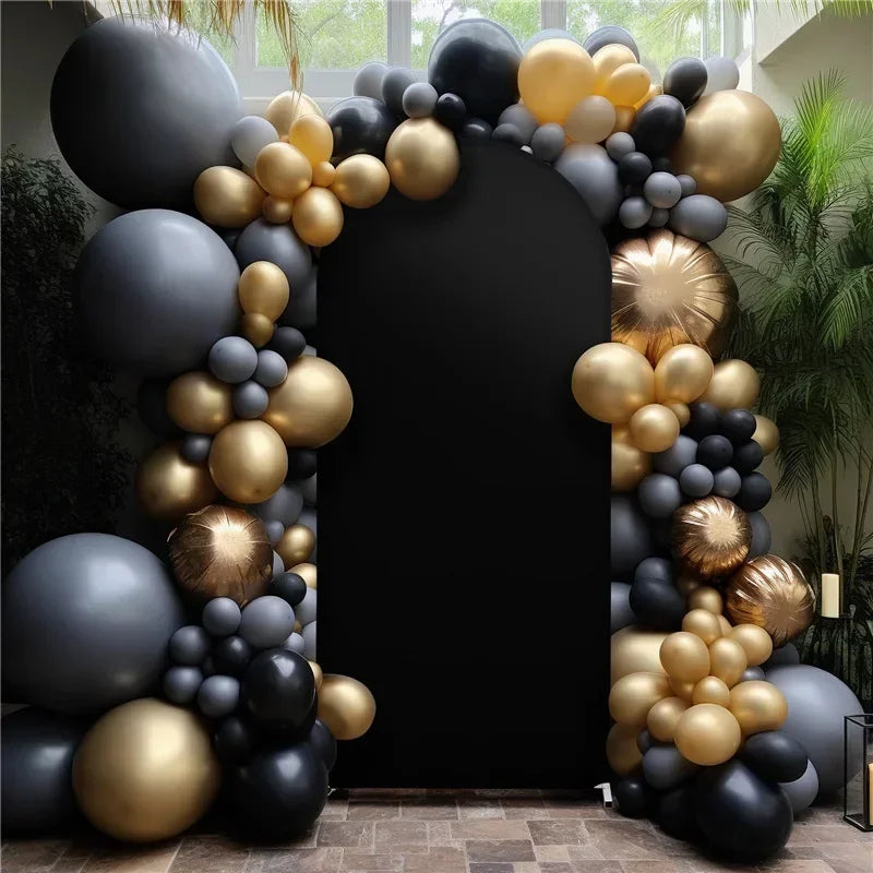 A dark gray and gold balloon arch backdrop cover decorated with round balloons and greenery.