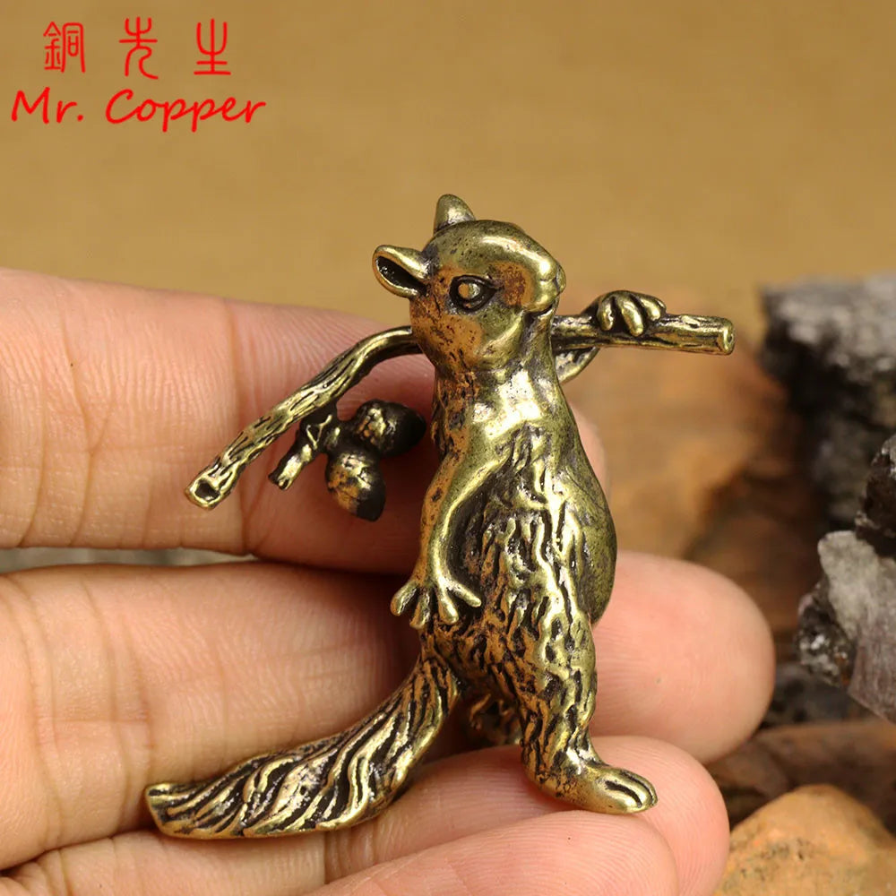 A brass squirrel figurine with a bushy tail is held in a person's hand against a natural background.
