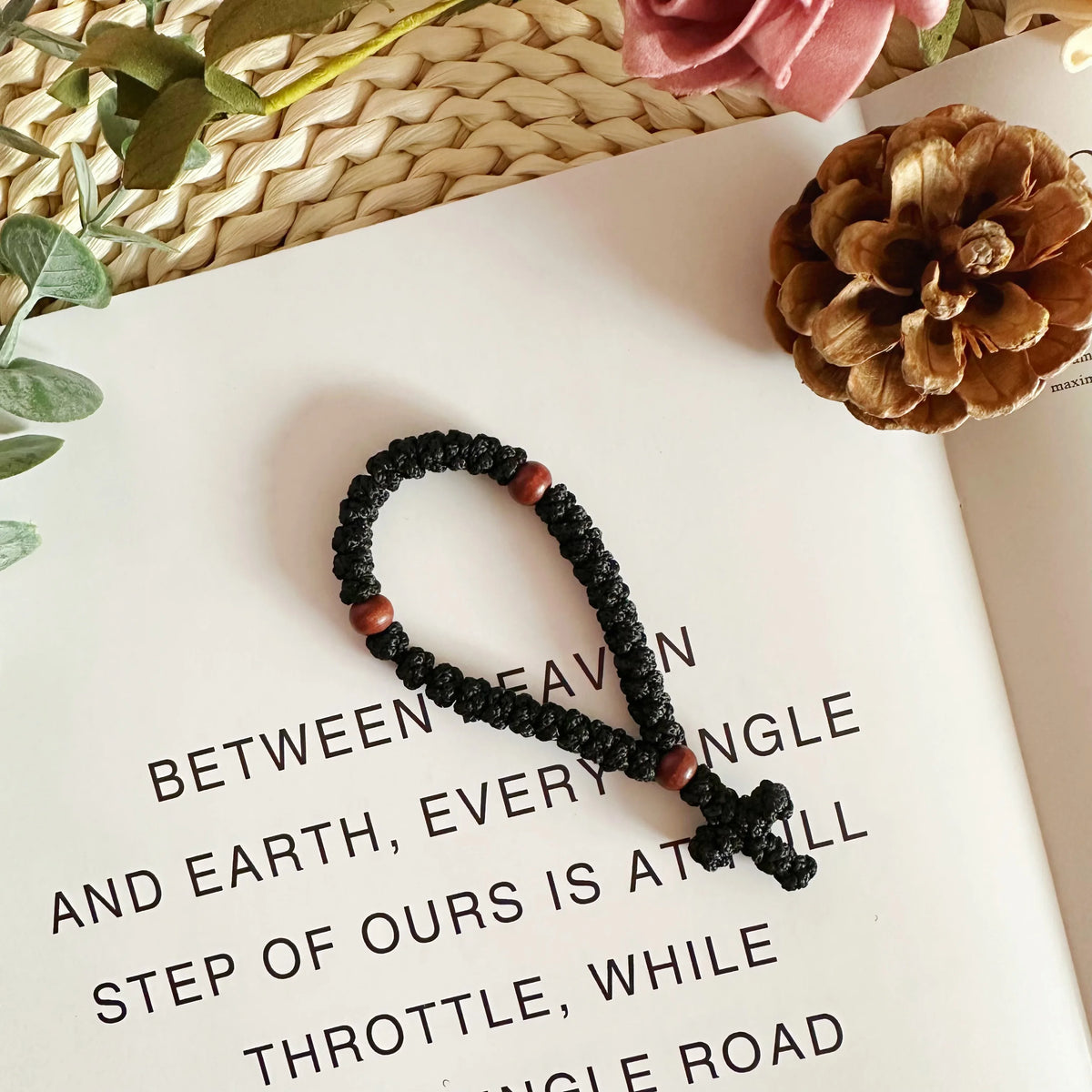 A black prayer rope with a wooden cross charm is displayed on a white page next to text.