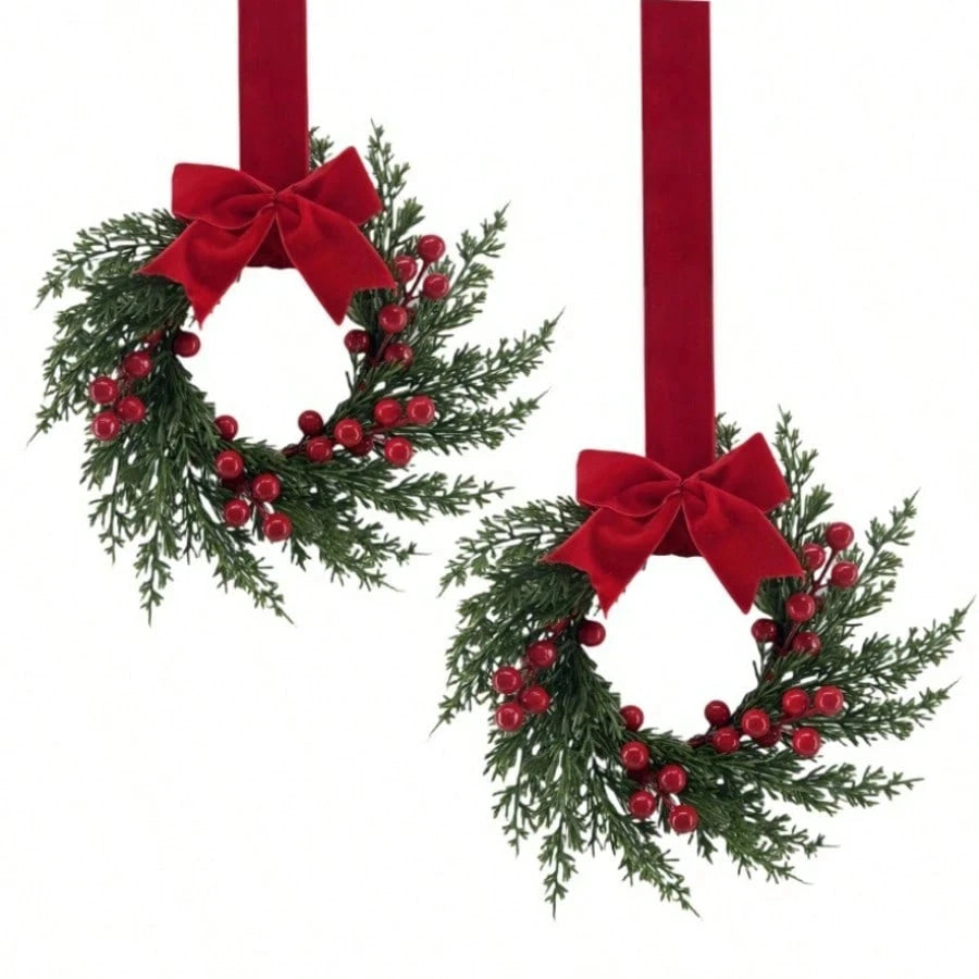 Set of two festive Christmas wreaths with green foliage and red berries tied with red ribbon for home decor