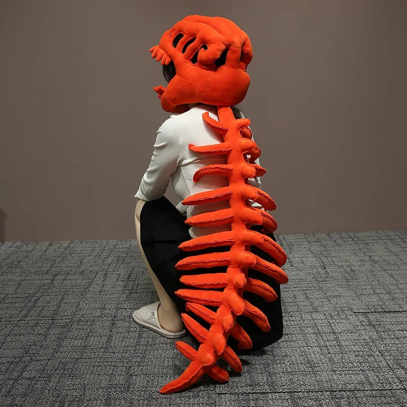 Peluche squelette de dinosaure orange avec chemise blanche et pantalon noir, présentée sur une surface grise.