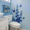 A bathroom wall features a blue floral and butterfly self-adhesive decal on the light blue wall above a toilet.