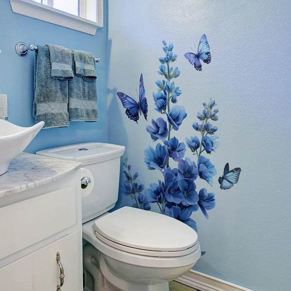A bathroom wall features a blue floral and butterfly self-adhesive decal on the light blue wall above a toilet.