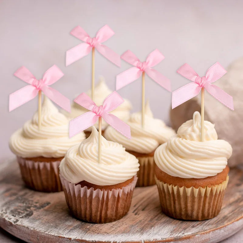 A collection of cupcakes topped with pink bow decorations arranged on a wooden surface.