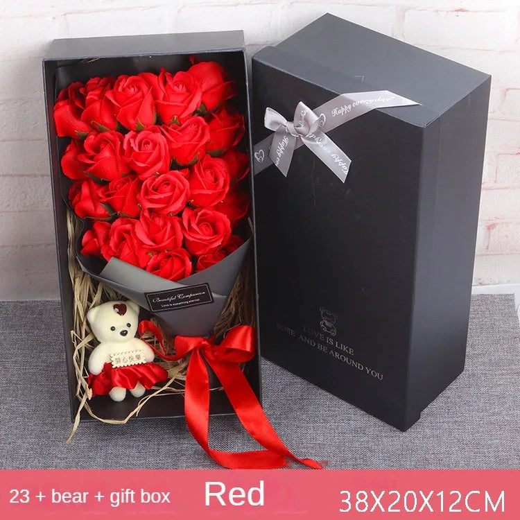 A gift box of red roses and a teddy bear is displayed on a gray surface.