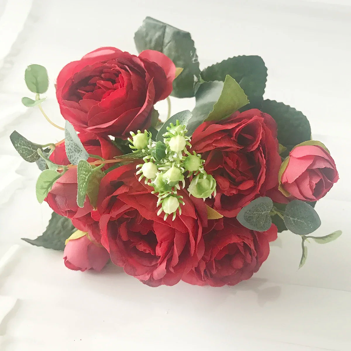 A bouquet of deep red silk roses and green leaves with small white filler flowers.