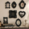 A gallery wall display of black ornate picture frames featuring floral and landscape designs on a cream-colored wall.