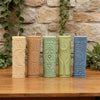 Five cylindrical silicone candle molds in pastel green and beige tones with celestial designs displayed on a wooden surface.