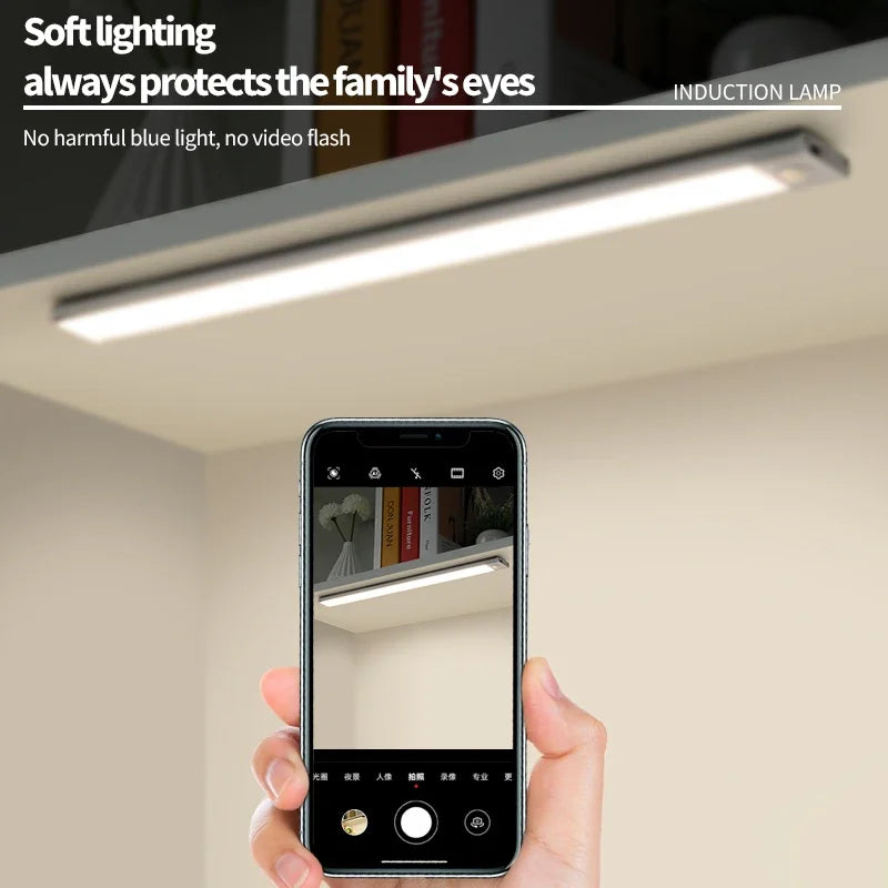 A hand holds a smartphone displaying an induction lamp light fixture installed under a cabinet.