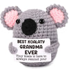 A gray crochet koala plush toy with pink ears and a tag that reads Best Koalaty Grandma Ever
