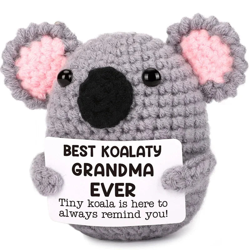 A gray crochet koala plush toy with pink ears and a tag that reads Best Koalaty Grandma Ever