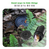 A black watering can key hider is partially hidden among leaves and dirt in an outdoor setting.