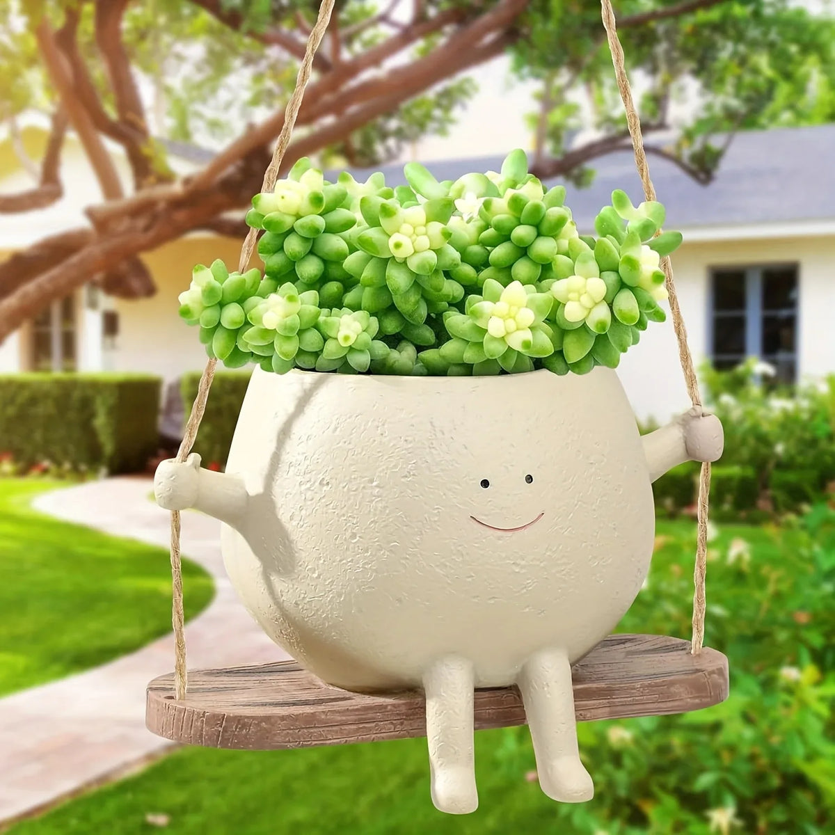 A white resin succulent planter with a smiling face is hanging from a wooden swing base outdoors.