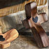 A wooden comfort prayer cross with a heart carved into it rests on a wooden tray.
