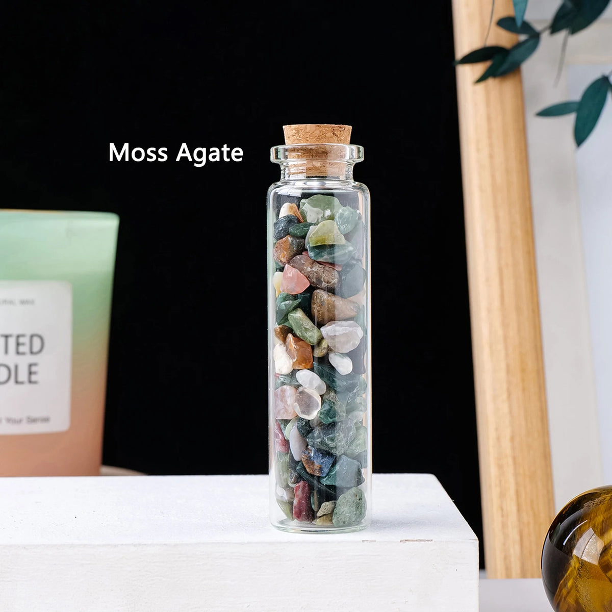 A glass bottle filled with various colored moss agate crystals displayed on a white surface.