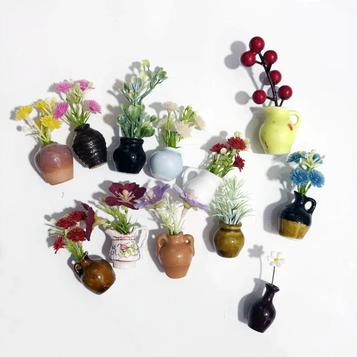 A collection of mini ceramic vases with artificial flowers in various colors and textures arranged on a white background.