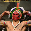A portrait of Alex Pereira with a vibrant feathered headdress and tattoos, set against a dark background.