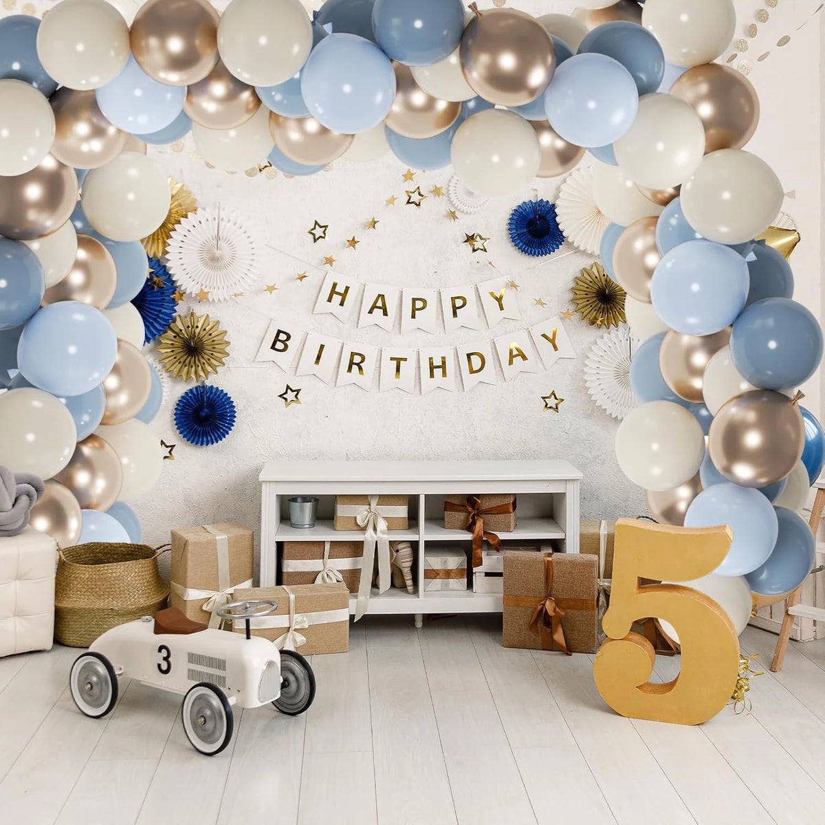 A wall decorated with a balloon arch and lettering spelling out Happy Birthday, featuring muted blue, gold, and white balloon