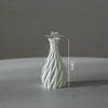 A white ceramic vase with a swirling, ribbed texture is shown against a gray background.