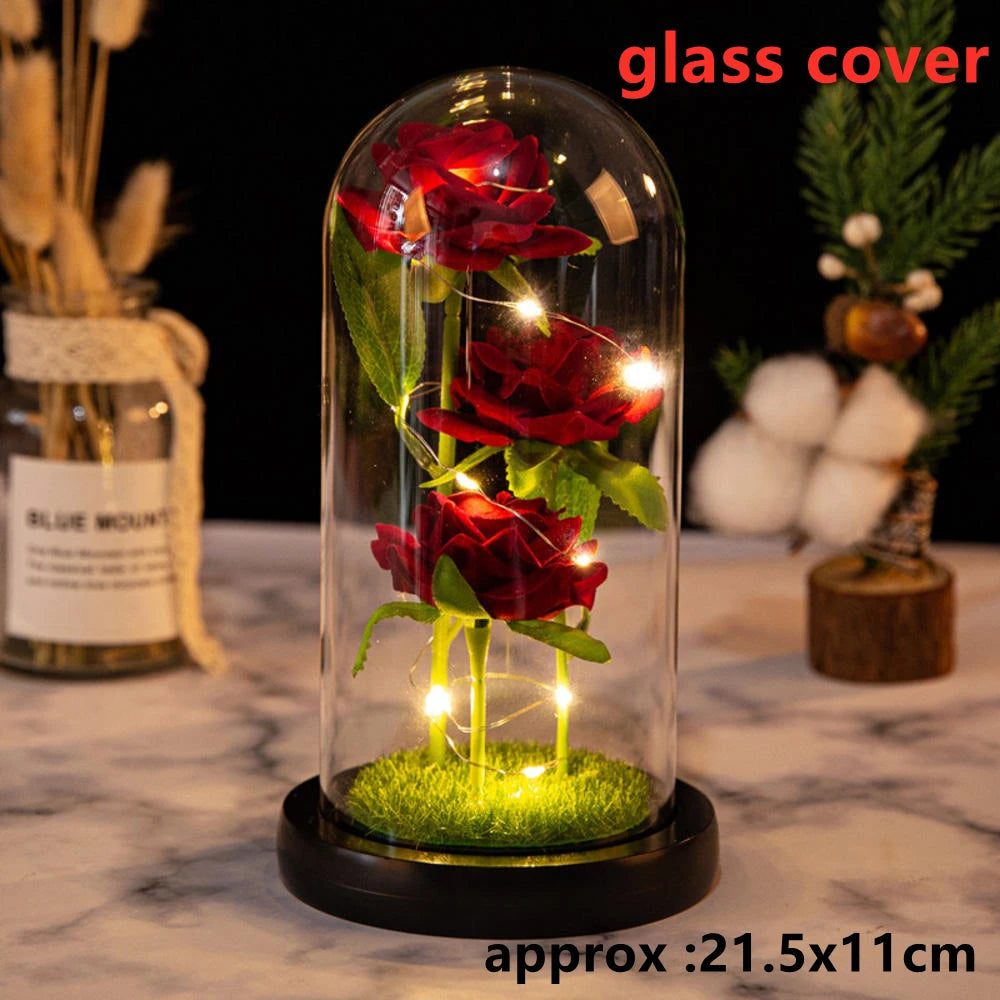 A glass dome display featuring red artificial roses illuminated by glowing LED lights on a moss base.