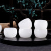 A set of four white crystal agate healing bowls displayed on a dark surface with green foliage in the background.
