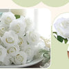 A close-up of a bouquet of white velvet artificial roses with green leaves and bendable stems.