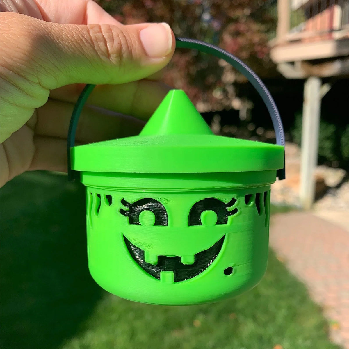 A hand holds a bright lime green miniature pumpkin Halloween bucket for treats and decor with a smiling face.