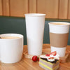 Three white disposable paper coffee cups are displayed on a wooden surface with a strawberry.