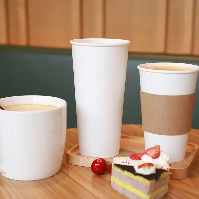 Three white disposable paper coffee cups are displayed on a wooden surface with a strawberry.