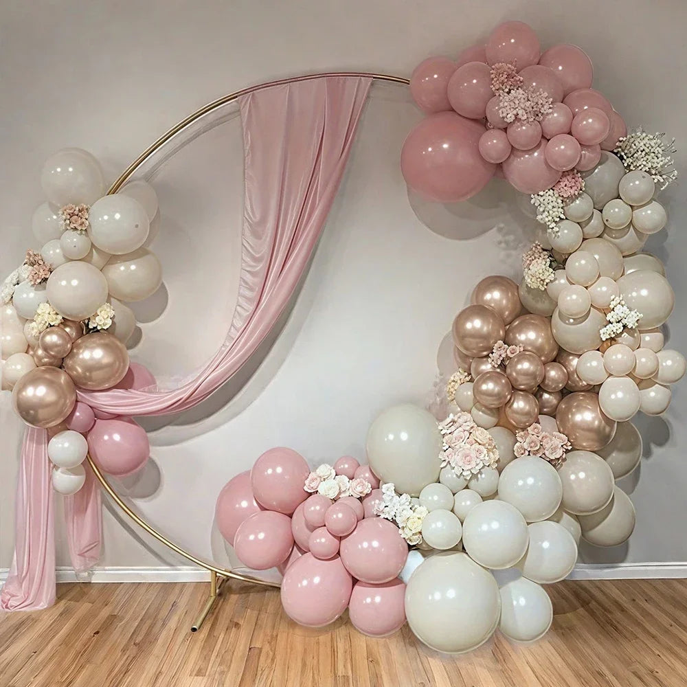 A decorative balloon arch featuring pink, sand, and gold balloons against a white wall.