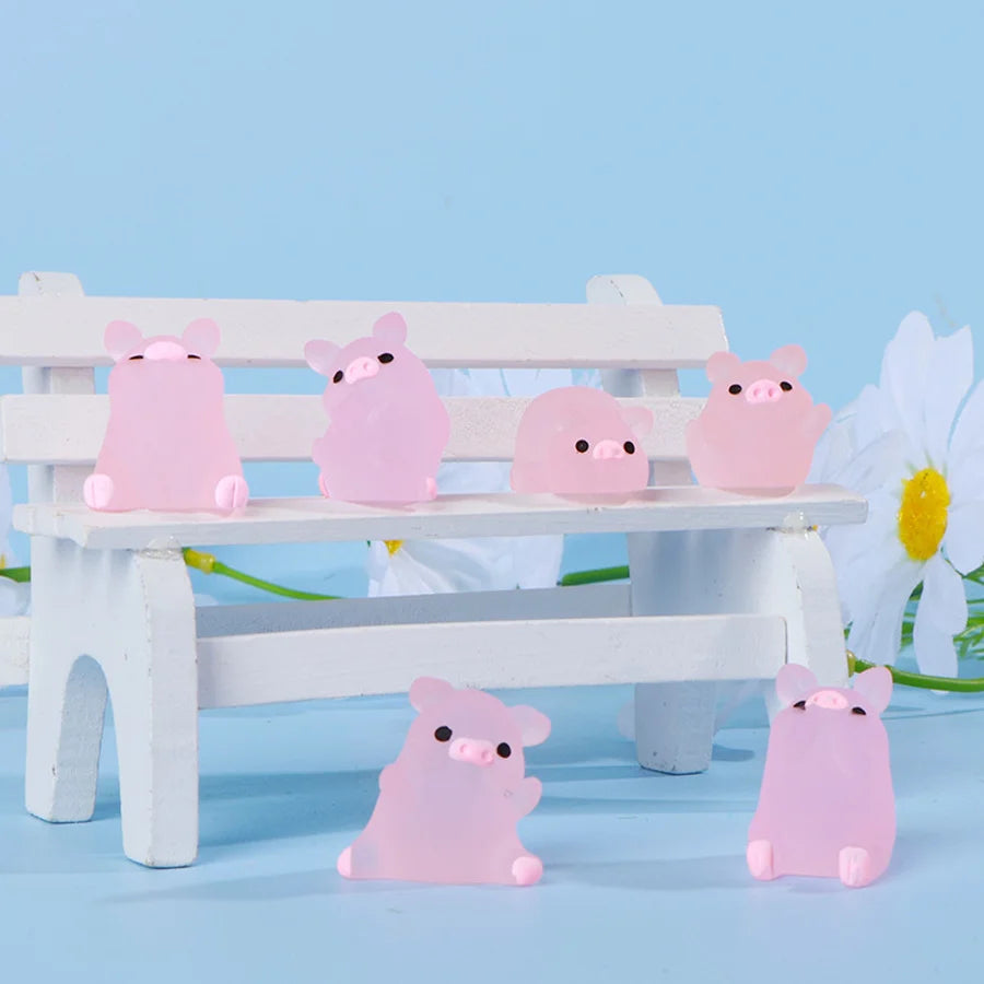 A collection of pink glow-in-the-dark mini pig figurines displayed on a white wooden bench against a light blue background.