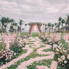 A pink and white floral aisle decorated with silk rose petals leading down a grassy path for a wedding ceremony.