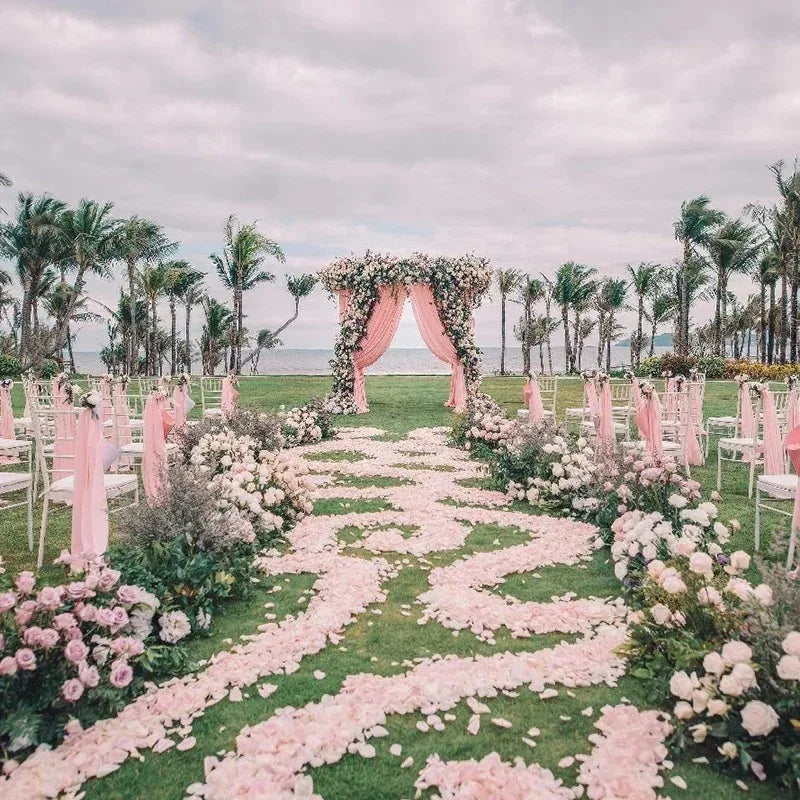 A pink and white floral aisle decorated with silk rose petals leading down a grassy path for a wedding ceremony.