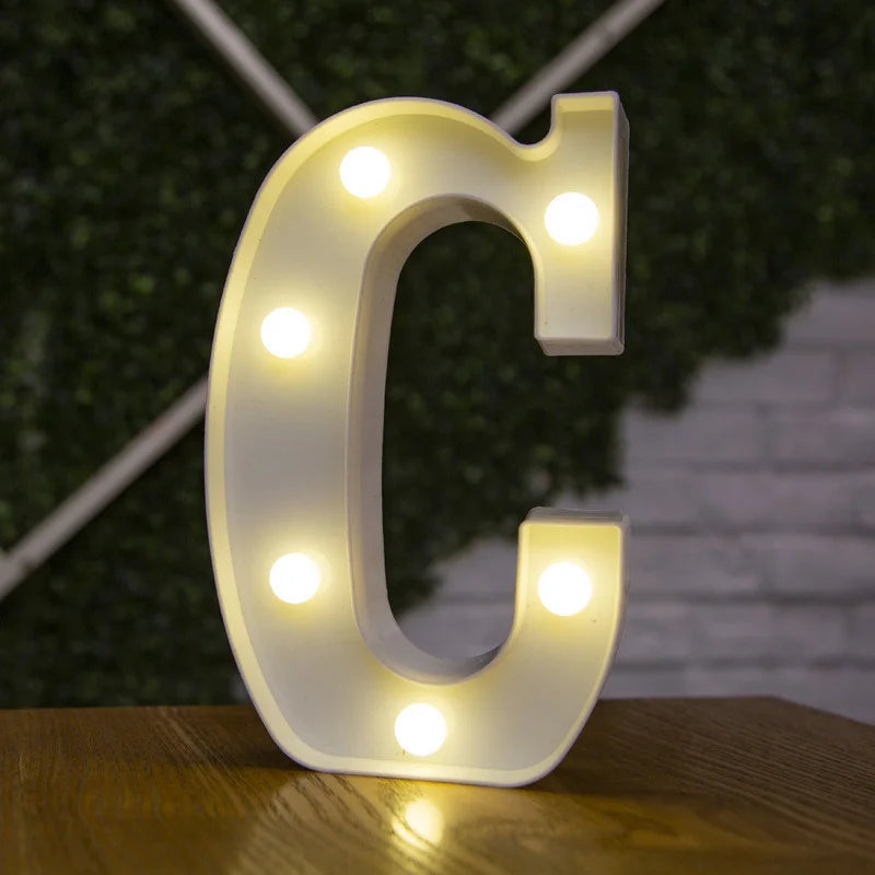 A glowing white alphabet letter C made of LED lights resting on a wooden surface.